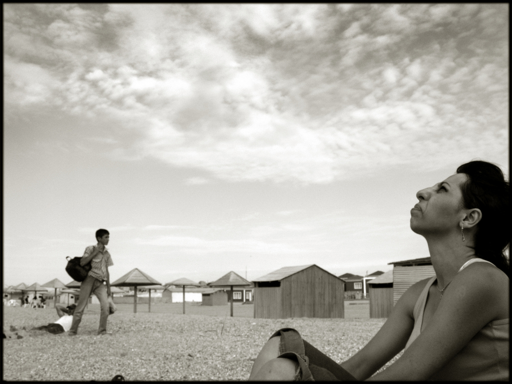 A man looking up to the sky on a beach with beach huts in the background