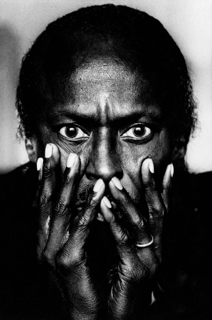 a black and white photo of miles Davis with his hands over his mouth