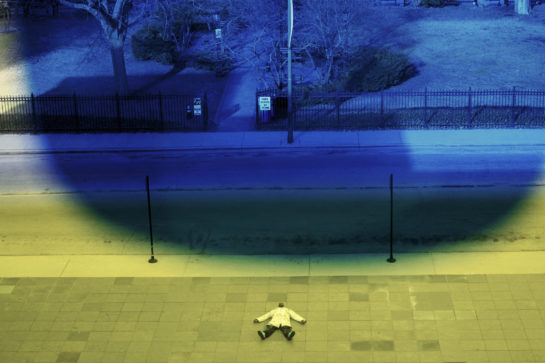 a blue light in a park and a man lying on the floor under a green light