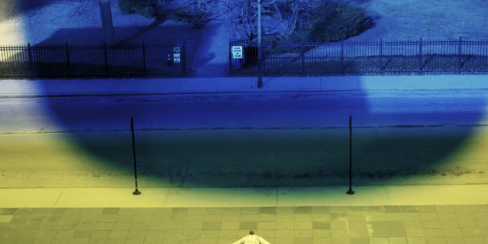 a blue light in a park and a man lying on the floor under a green light