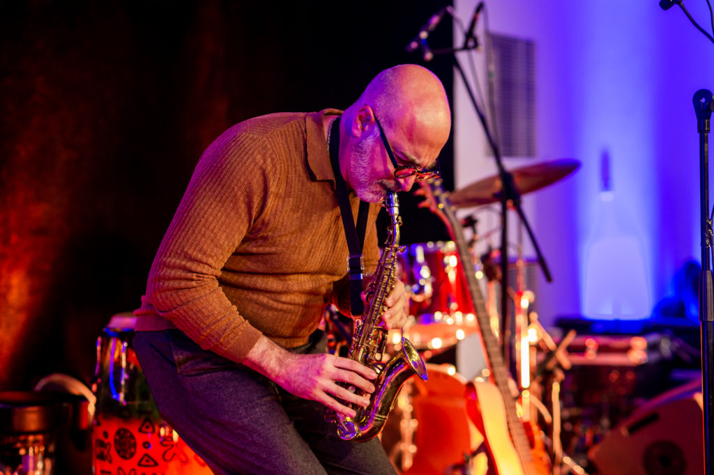 A man in a camel coloured polo shirt playing the saxophone 