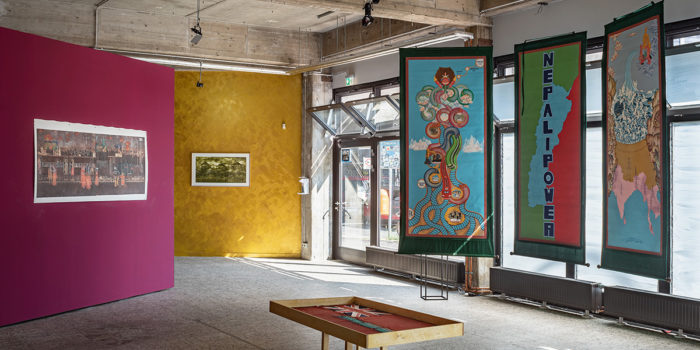 An art gallery with pink and yellow walls and a piece saying 'Nepal Power'