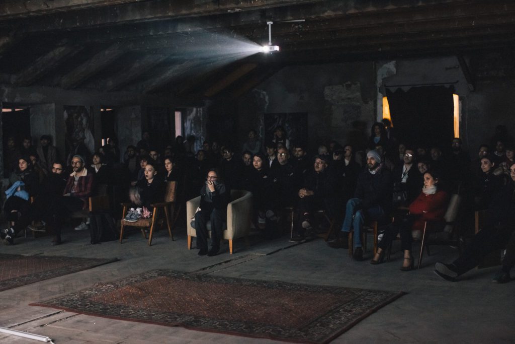 A group of young people sitting on chairs watching. projection