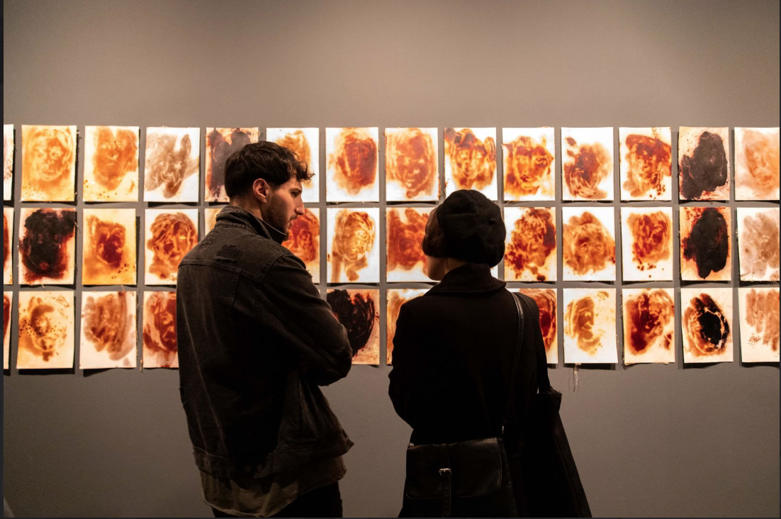 A girl and a boy dressed in black looking at orange artworks on a wall