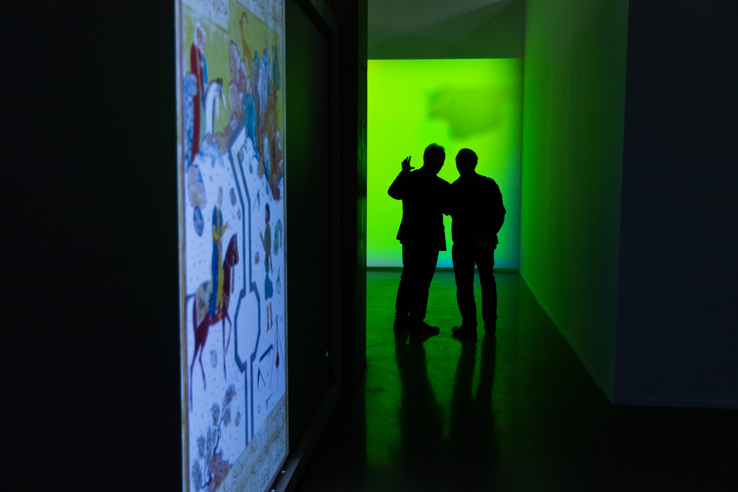people standing in a dark corridor with a green light looking at an artwork