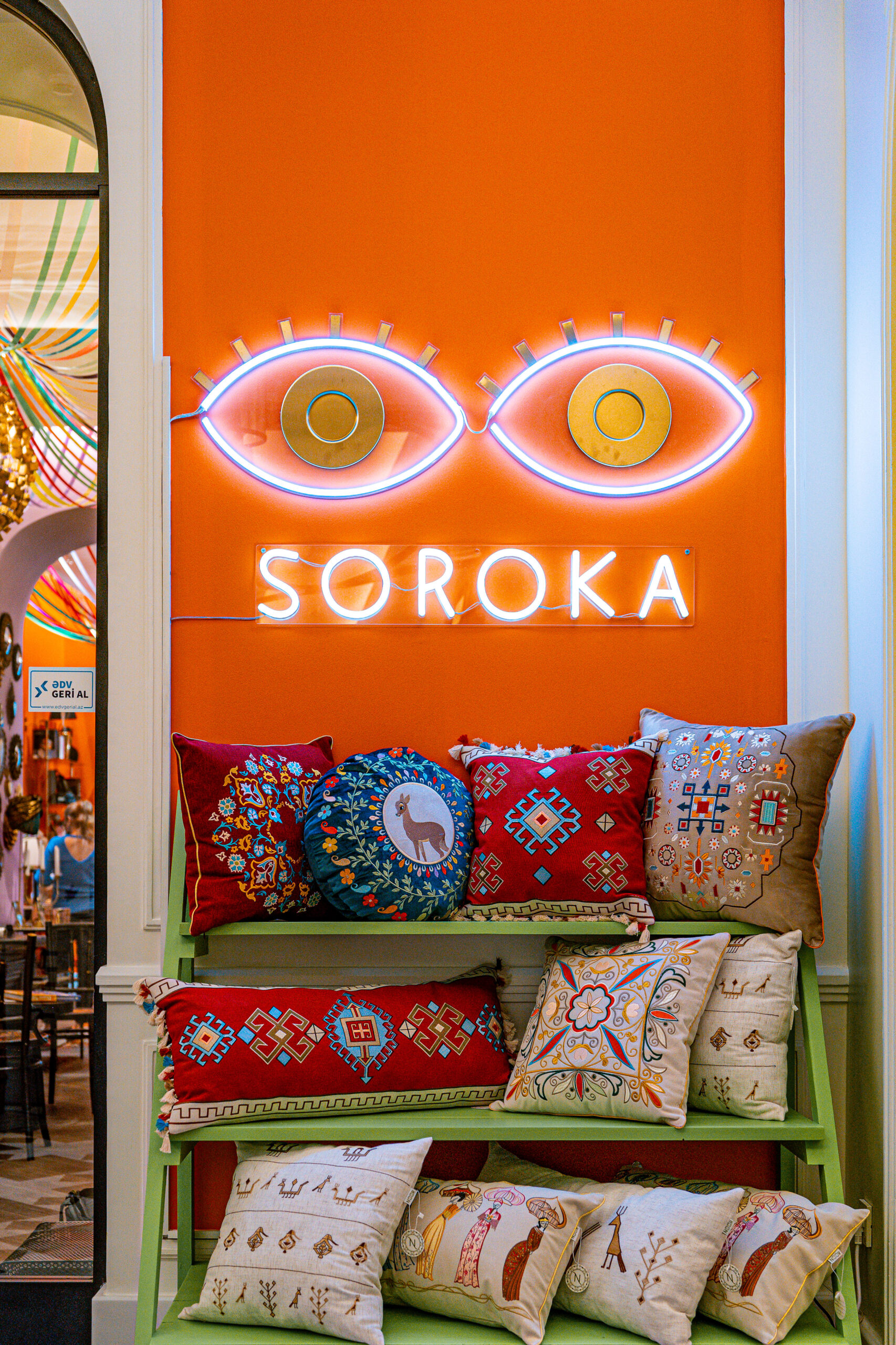 An orange wall with light up eyes on the wall and pillows on a green shelf