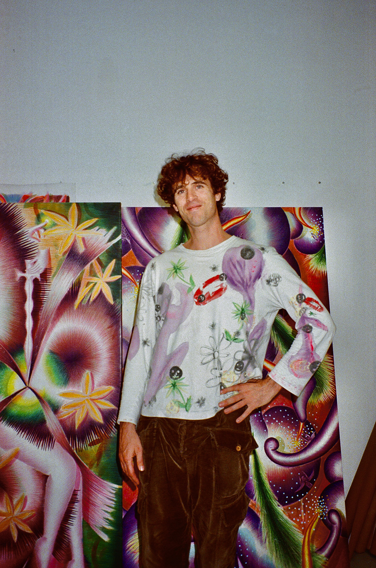 Arists in a white t-shirt in his studio, around his canvases of colourful pencil drawings
