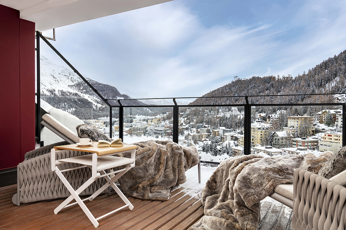 fur blankets on chairs on a terrace overlooking mountains covered in snow