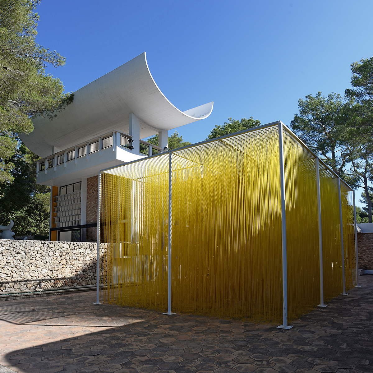 White building with yellow art installation , blue sky and trees