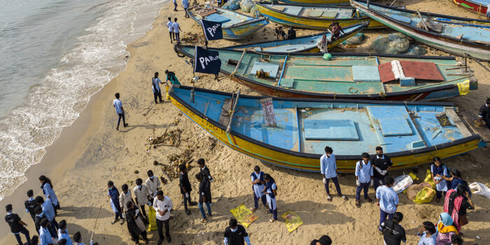 Blue boats and lots of people on sandy beach by sea